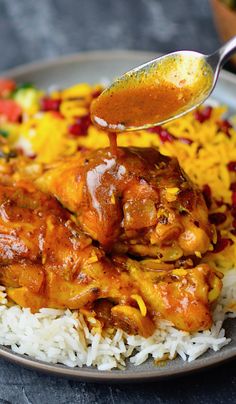 a spoon is being used to stir chicken over rice on a plate with other food