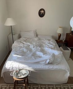 an unmade bed sitting in a bedroom next to a table with a lamp on it