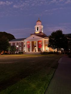 a building with a clock tower lit up in the night sky at dusk, on a grassy lawn