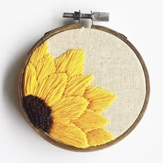 a cross stitch sunflower is shown on a white surface with an embroidered hoop hanging from it's side