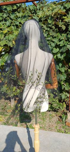 a veiled mannequin in front of some bushes