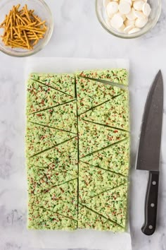 green cake with white chocolate and sprinkles on top next to a knife