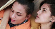 two women are looking at something on their cell phone while wearing ear rings and scarves