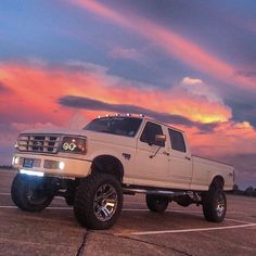 a white pickup truck parked in a parking lot at sunset with the sun going down