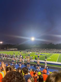 a group of people standing on top of a football field at night with lights in the background