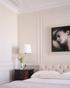 a white bed sitting in a bedroom next to a lamp and painting on the wall