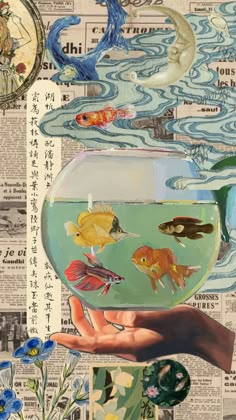 a hand holding a fish in a bowl filled with water and surrounded by blue flowers