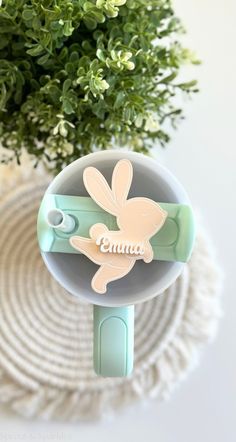 a cup with a bunny on it sitting in front of a potted plant and the name ema