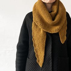 a woman wearing a knitted scarf in mustard yellow and black, standing against a white wall