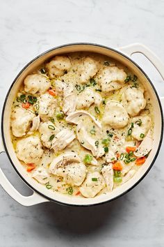 a pot filled with dumplings and vegetables on top of a white countertop next to a wooden spoon