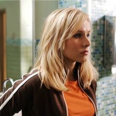 a woman in an orange shirt and brown jacket is looking at something on the wall