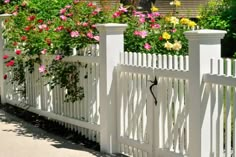 a white picket fence with pink and yellow flowers growing on it's sides in front of a house