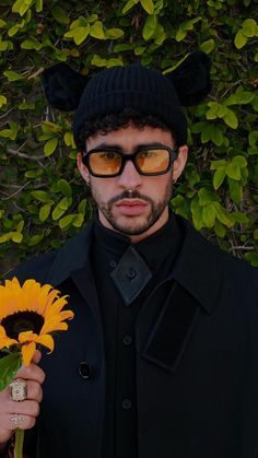 a man wearing sunglasses and a hat holding a sunflower