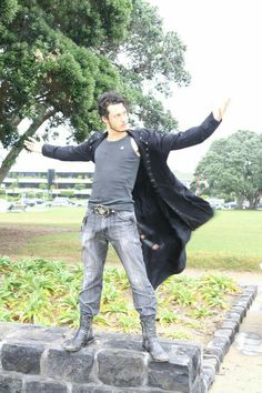 a man standing on top of a brick wall next to a lush green park filled with trees