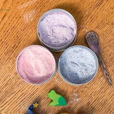 three tins filled with different colored powder on top of a wooden table next to toys