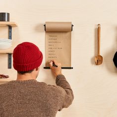 a man in a red hat writing on a piece of paper next to some shelves