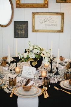 the table is set with white and gold place settings, black napkins, and candles