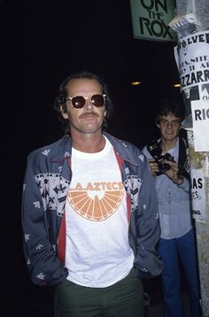 a man wearing sunglasses standing next to a pole