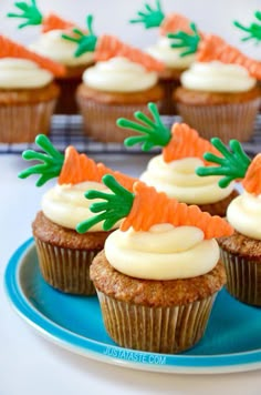 carrot cupcakes with white frosting and green sprinkles on a blue plate