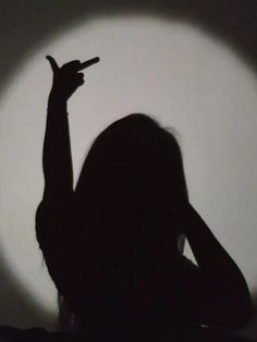 the silhouette of a woman holding her hand up in front of a circular shadow on a wall