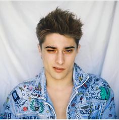 a young man with short hair wearing a denim shirt and looking at the camera while standing in front of a white backdrop