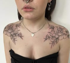 a woman with tattoos on her chest wearing a black dress and nose piercings is looking at the camera