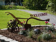 a welcome sign in the middle of a flower bed with flowers and a wheel on it