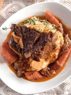 a white bowl filled with meat and potatoes covered in gravy on top of a table