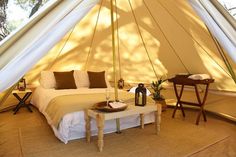 a bed sitting inside of a tent next to a table and lamp on top of a rug