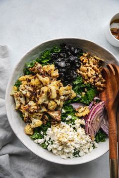 a white bowl filled with different types of food next to a wooden utensil