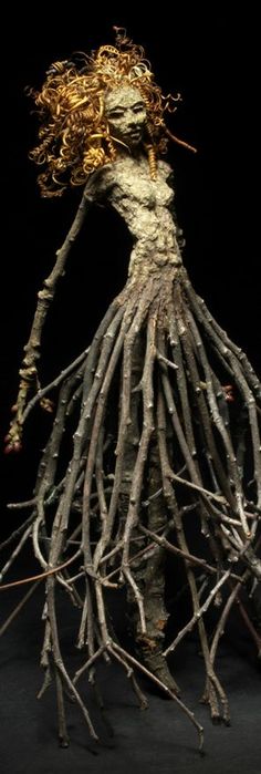 a woman made out of sticks and twigs on a black background with the roots exposed