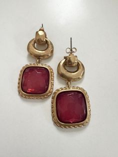 two pairs of gold and red earrings on a white surface with one earring in the shape of a square