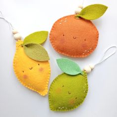 three felt oranges with green leaves on them hanging from white string and bead