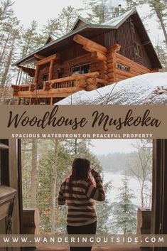 a woman standing in front of a window looking out at the woods and a cabin