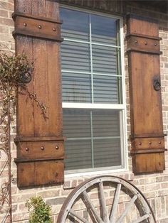 an old wagon wheel sits in front of a brick building with shutters and windows