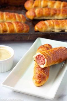 two sausage rolls on a white plate next to some breadsticks and dipping sauce