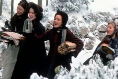 four women are walking through the snow carrying plates and drinks in their hands as they look at something off to the side