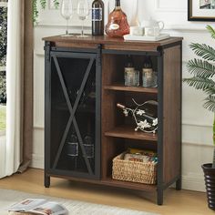 an open cabinet with wine glasses and bottles on top in front of a potted plant