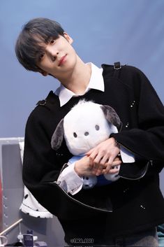 a young man holding a stuffed animal in his hands while wearing a black jacket and white shirt