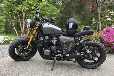 a black motorcycle parked on top of a gravel road in front of trees and flowers