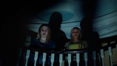 two women are standing in the dark with their shadows on the wall and behind them is a railing