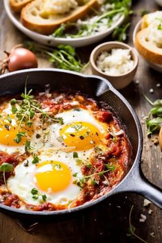 two fried eggs in a skillet with bread and garlic on the side, ready to be eaten