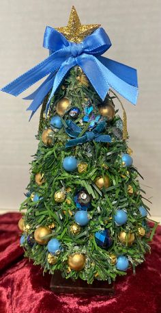 a small christmas tree with blue and gold ornaments on it's top, sitting on a red velvet surface