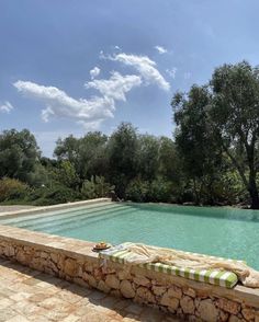 an empty swimming pool in the middle of a stone patio area with green trees and blue sky