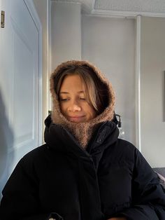 a woman in a black jacket is looking down at her cell phone while wearing a fur hood