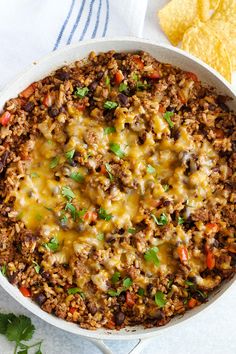 a casserole dish with ground beef, cheese and tortilla chips on the side