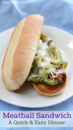 meatball sandwich with pickles and cheese on a white plate, sitting on a blue table cloth