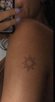 a woman with a sun tattoo on her arm holding a cell phone and taking a selfie