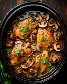 chicken with mushrooms and parsley in a black crock pot on a wooden table