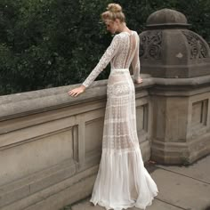 a woman in a white dress leaning against a stone wall with her hand on the side